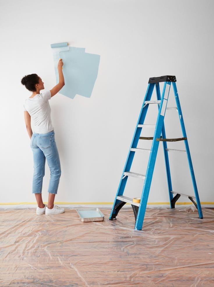 Living room with modern furniture including a gray armchair, a blue armchair, a sofa, and a round glass coffee table on a rug in a bright room with white paneled walls and large window